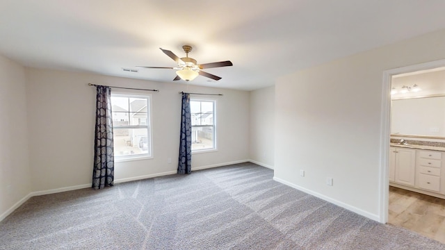 unfurnished bedroom featuring sink, ensuite bath, light carpet, and ceiling fan