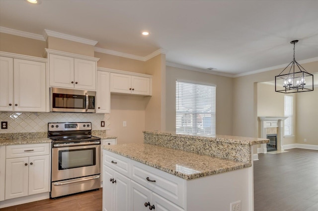 kitchen featuring tasteful backsplash, white cabinets, appliances with stainless steel finishes, ornamental molding, and wood finished floors