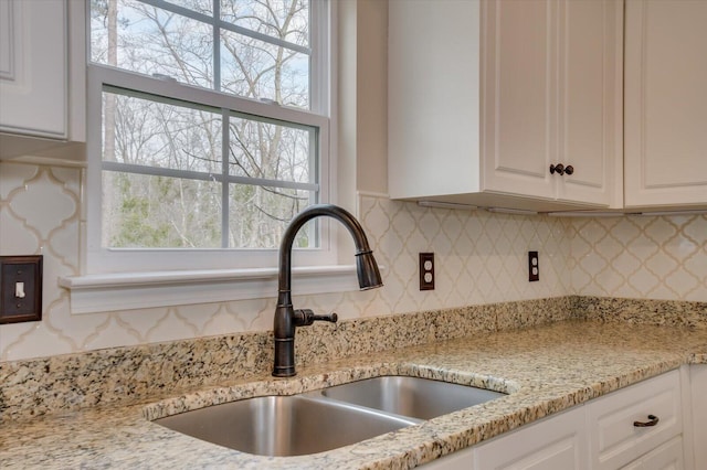 kitchen featuring light stone counters, white cabinetry, backsplash, and a sink