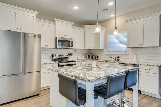 kitchen with appliances with stainless steel finishes, light stone counters, a kitchen island, decorative light fixtures, and white cabinetry