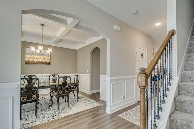 dining space featuring beam ceiling, coffered ceiling, an inviting chandelier, ornamental molding, and hardwood / wood-style flooring