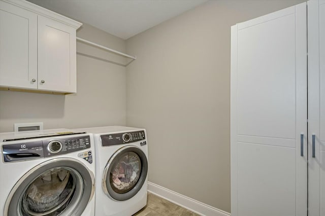 clothes washing area featuring washer and dryer, light tile patterned flooring, and cabinets