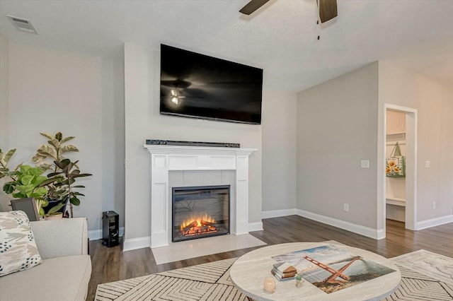 living room featuring a tile fireplace, ceiling fan, and dark wood-type flooring