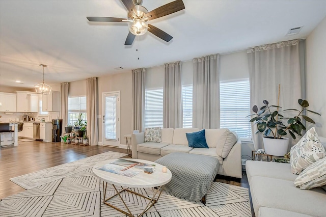 living room with light wood-type flooring, ceiling fan with notable chandelier, and a healthy amount of sunlight