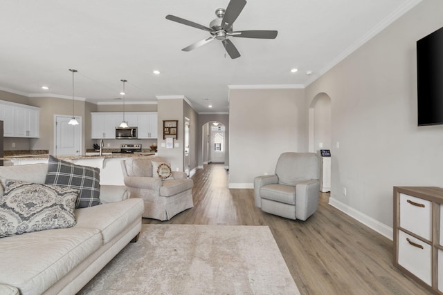 living area with arched walkways, baseboards, ornamental molding, recessed lighting, and light wood-style flooring
