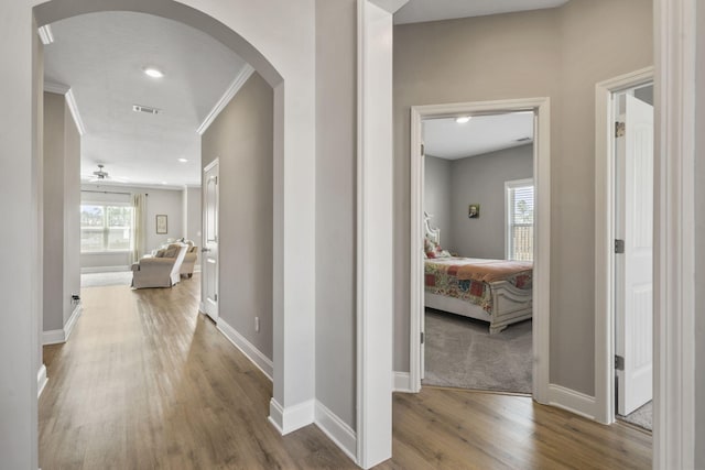 hall with visible vents, arched walkways, wood finished floors, baseboards, and ornamental molding