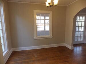 spare room featuring ornamental molding, an inviting chandelier, and dark wood-type flooring