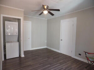 unfurnished room featuring crown molding, stacked washer and dryer, ceiling fan, and dark wood-type flooring