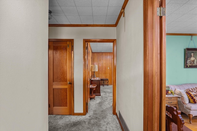 corridor with ornamental molding, light colored carpet, and wood walls