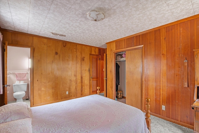 bedroom with ensuite bath, wooden walls, light colored carpet, and a closet