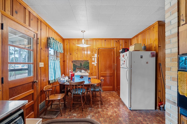 kitchen with white refrigerator, hanging light fixtures, and wood walls