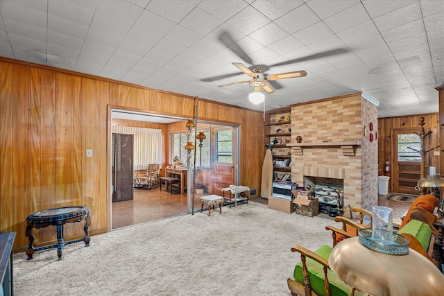 living room with a brick fireplace, wooden walls, ceiling fan, and carpet