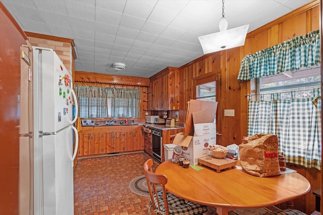 kitchen featuring wooden walls, sink, hanging light fixtures, white fridge, and range