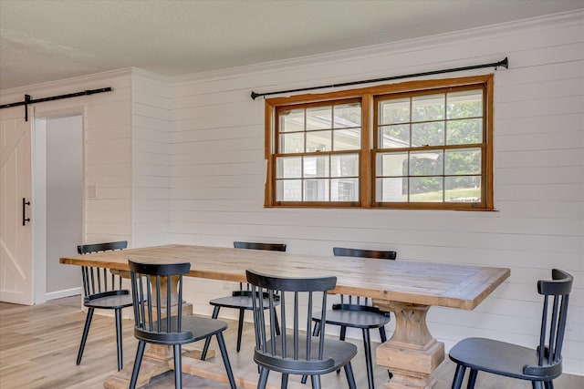 dining room with a barn door, ornamental molding, light wood-style flooring, wood walls, and breakfast area