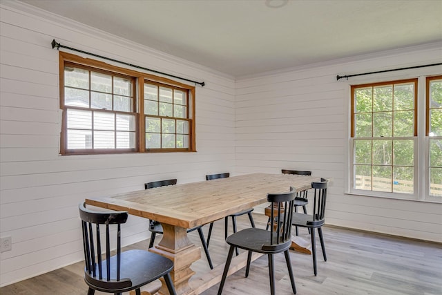 dining space with plenty of natural light, ornamental molding, wood walls, and light wood-style flooring
