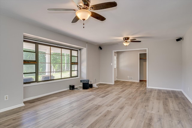 unfurnished room with ceiling fan, light wood-type flooring, baseboards, and a wood stove