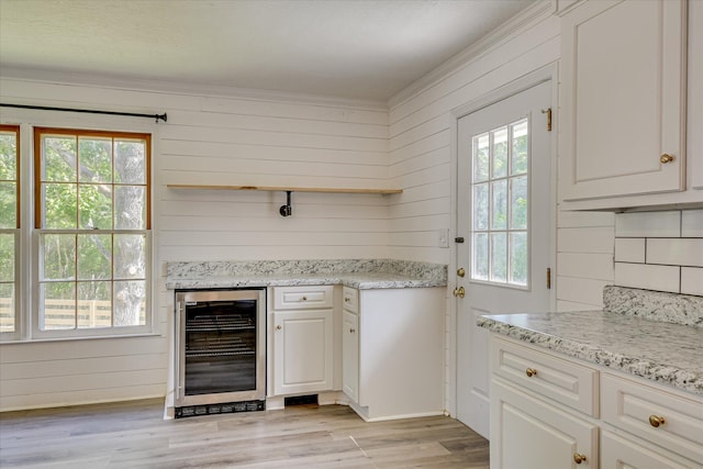 bar area featuring wine cooler, plenty of natural light, light wood-style flooring, wooden walls, and crown molding
