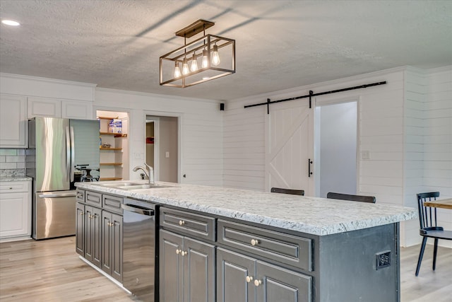 kitchen with appliances with stainless steel finishes, a barn door, light wood-style floors, a sink, and a textured ceiling