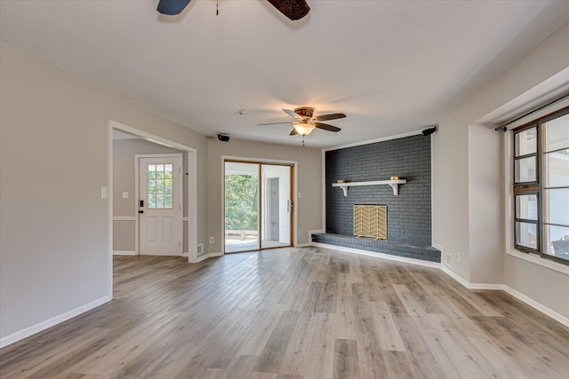 unfurnished living room featuring ceiling fan, a brick fireplace, wood finished floors, and baseboards
