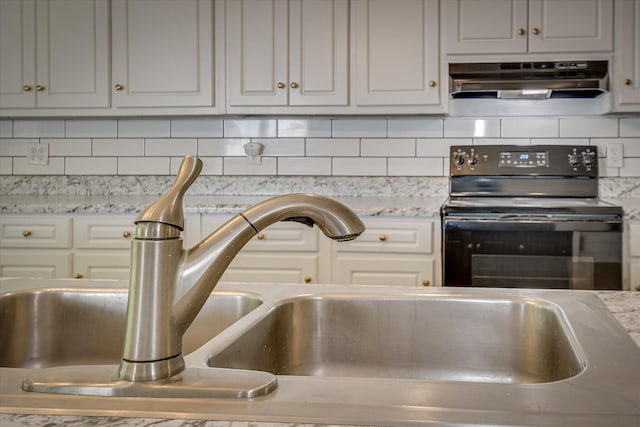 kitchen view of electric range, under cabinet range hood, a sink, decorative backsplash, and light stone countertops