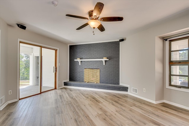 unfurnished living room with wood finished floors, healthy amount of natural light, ceiling fan, and a brick fireplace