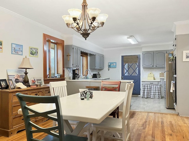 dining space with an inviting chandelier, sink, crown molding, and light wood-type flooring