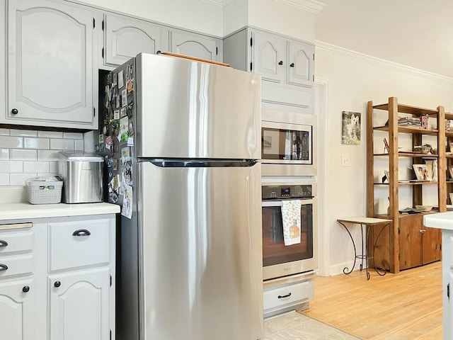 kitchen featuring white cabinets, backsplash, stainless steel appliances, crown molding, and light hardwood / wood-style flooring