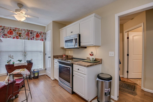 kitchen with light wood-style flooring, appliances with stainless steel finishes, white cabinetry, dark stone countertops, and baseboards