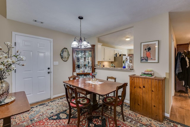 dining space featuring baseboards, a chandelier, visible vents, and light wood-style floors