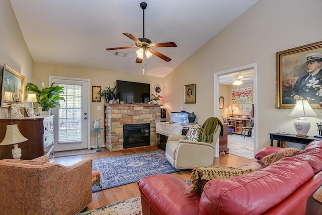 living room with light wood finished floors, visible vents, lofted ceiling, ceiling fan, and a stone fireplace