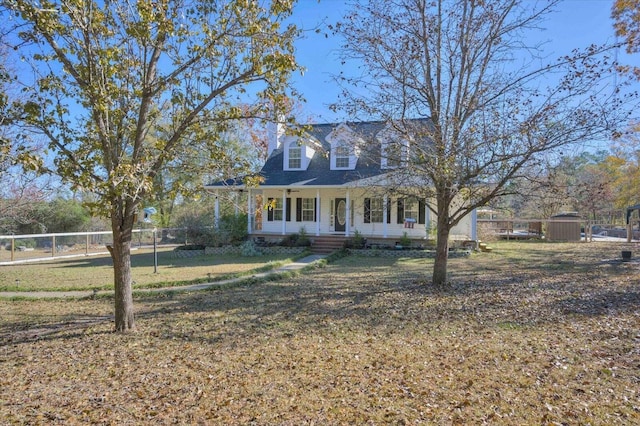 cape cod-style house featuring a front lawn, covered porch, and a storage shed