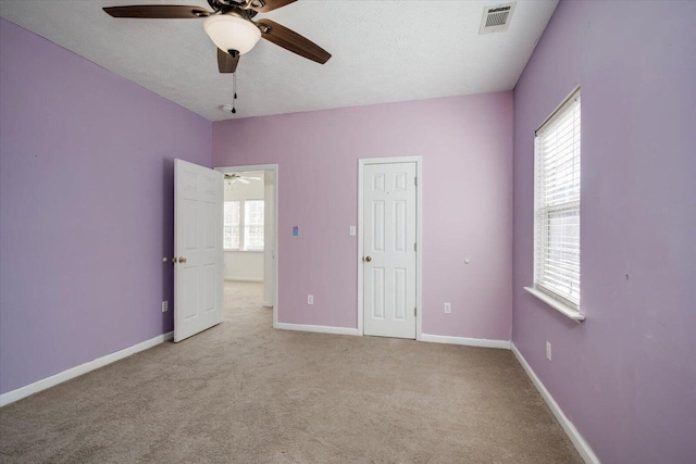 unfurnished bedroom featuring multiple windows, ceiling fan, light carpet, and a textured ceiling