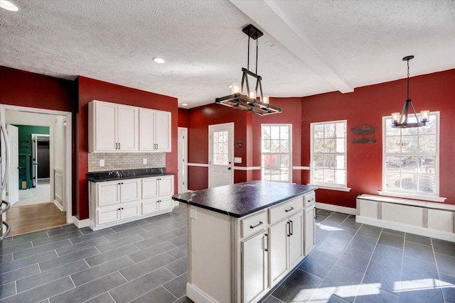 kitchen featuring white cabinets, decorative light fixtures, backsplash, and beamed ceiling