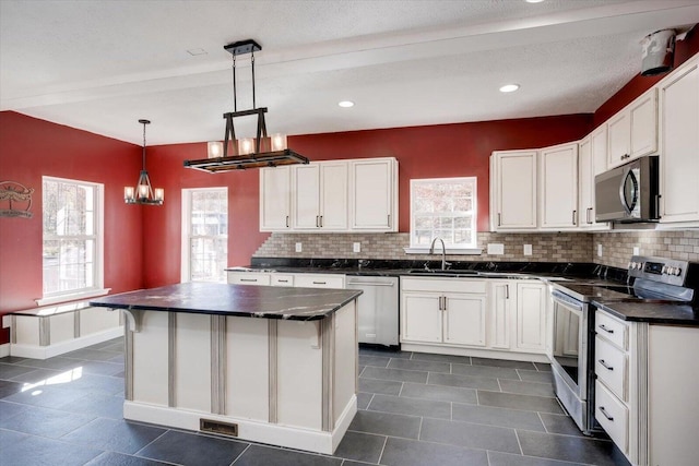 kitchen featuring backsplash, stainless steel appliances, decorative light fixtures, a center island, and white cabinetry