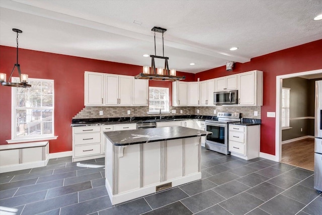 kitchen with appliances with stainless steel finishes, decorative light fixtures, a kitchen island, and white cabinetry