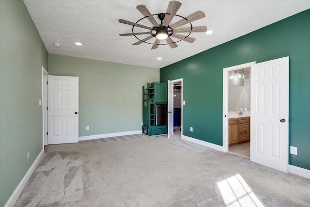 unfurnished bedroom with a textured ceiling, connected bathroom, light colored carpet, and ceiling fan