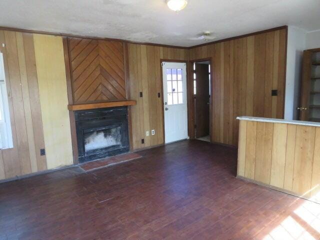 unfurnished living room with crown molding, a fireplace with raised hearth, wood walls, and wood finished floors