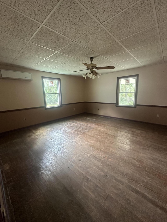 spare room featuring hardwood / wood-style floors, a drop ceiling, a wall mounted AC, and ceiling fan