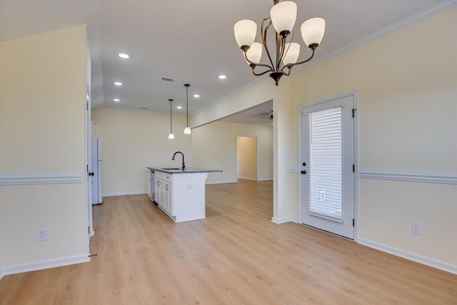 kitchen featuring decorative light fixtures, white cabinetry, sink, a kitchen island with sink, and crown molding