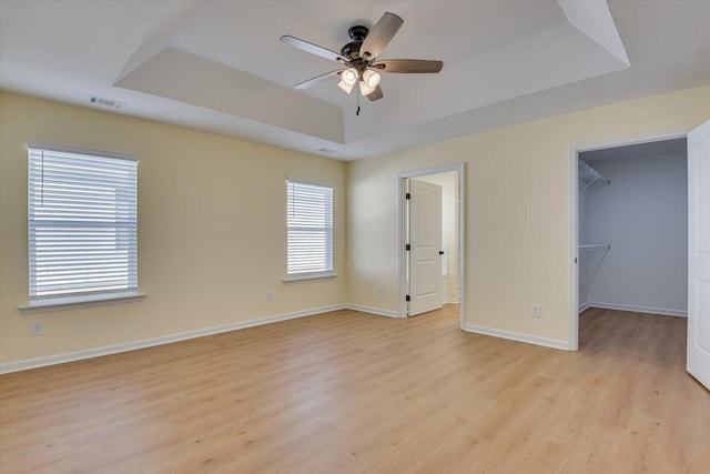 unfurnished bedroom featuring ceiling fan, a tray ceiling, light hardwood / wood-style floors, a walk in closet, and a closet