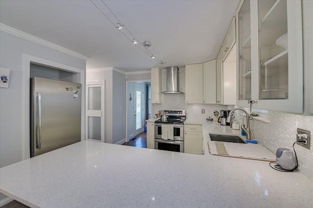 kitchen featuring wall chimney range hood, appliances with stainless steel finishes, a sink, backsplash, and light stone countertops