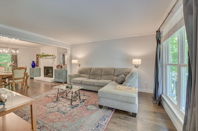 living room featuring crown molding, a chandelier, wood finished floors, baseboards, and a brick fireplace