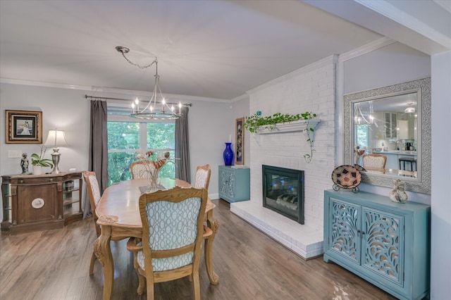 dining area featuring a chandelier, crown molding, wood finished floors, and a brick fireplace