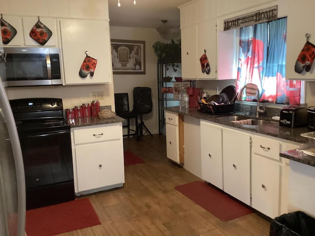 kitchen featuring sink, dark stone countertops, light wood-type flooring, black range with electric cooktop, and white cabinetry