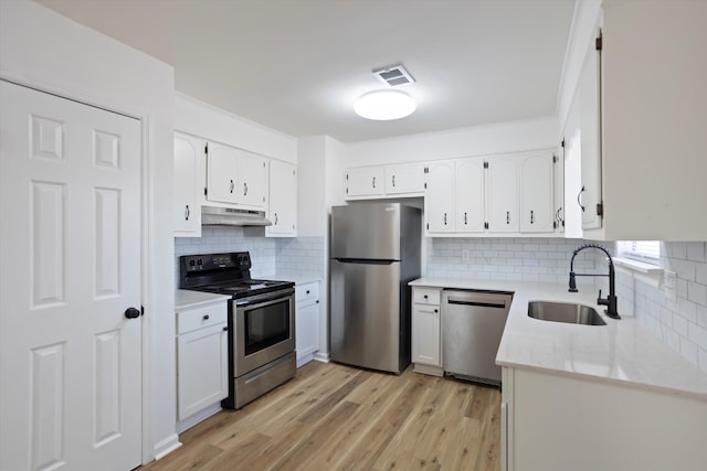 kitchen featuring light wood-style flooring, appliances with stainless steel finishes, white cabinets, a sink, and under cabinet range hood