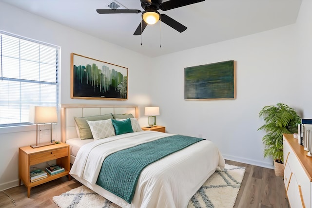 bedroom featuring ceiling fan, visible vents, baseboards, and wood finished floors