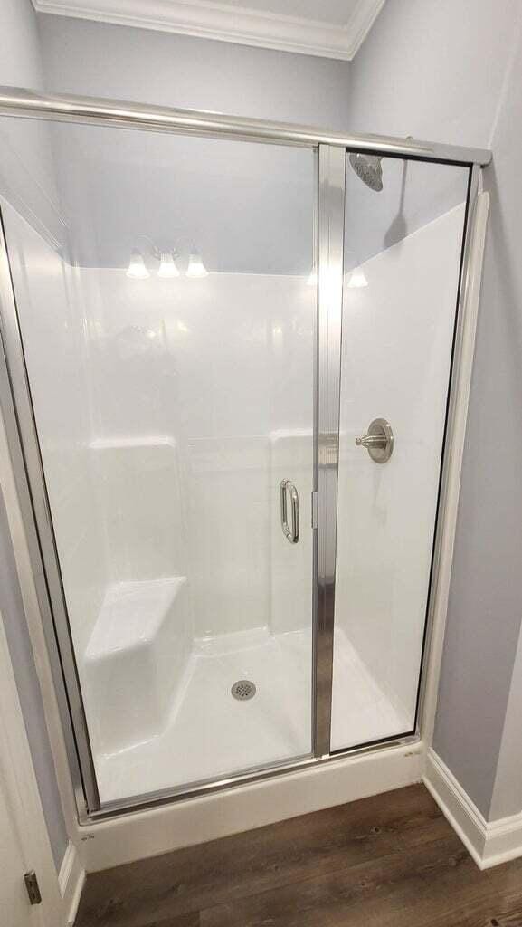 bathroom featuring wood-type flooring, crown molding, and a shower with shower door