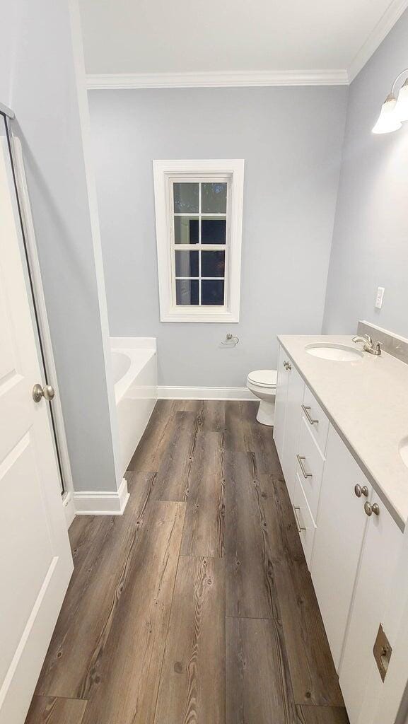 bathroom featuring crown molding, a bathing tub, vanity, wood-type flooring, and toilet