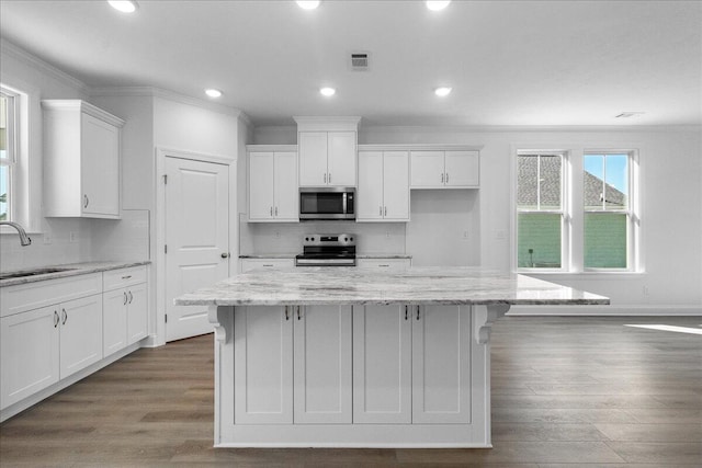 kitchen with white cabinetry, stainless steel appliances, a center island, and light stone countertops