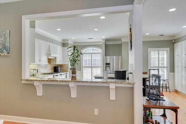 5407 Kiokee Ridge Rd, Evans, GA 30809 - kitchen featuring light stone countertops, stainless steel fridge with ice dispenser, premium range hood, a peninsula, and backsplash